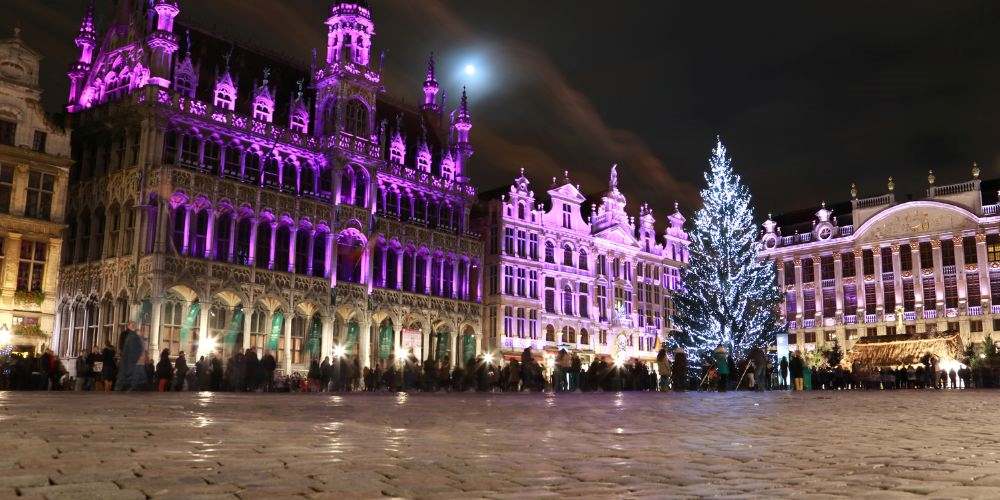 Tall old building with purple lights and crowd watching in front - best christmas markets in the world