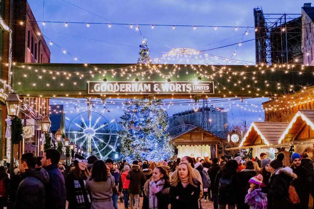 crowd with stalls in the side selling goodies and on top is christmas lights