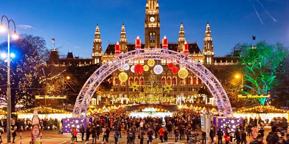Large old structure building at the back of a well light chirstmas market- best christmas markets in the world