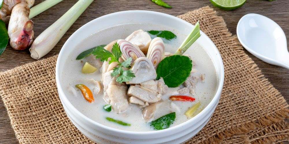 white soup with mushroom and green leaves in white dish - best thai food in thailand