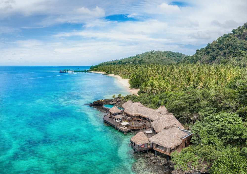 aerial view of a hotel made of nipa hut near bpdy of water and surrounded by trees